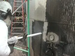 A man is spraying water on the wall of an industrial building.