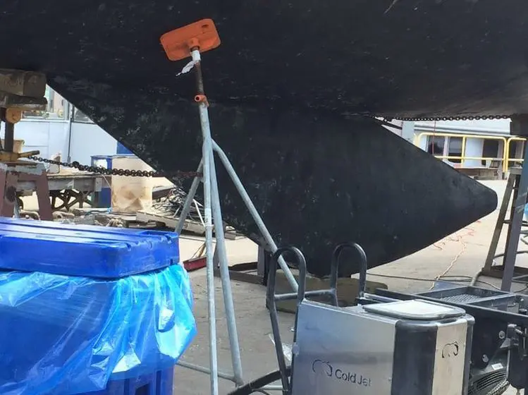 A black umbrella is sitting on top of a blue trash can.